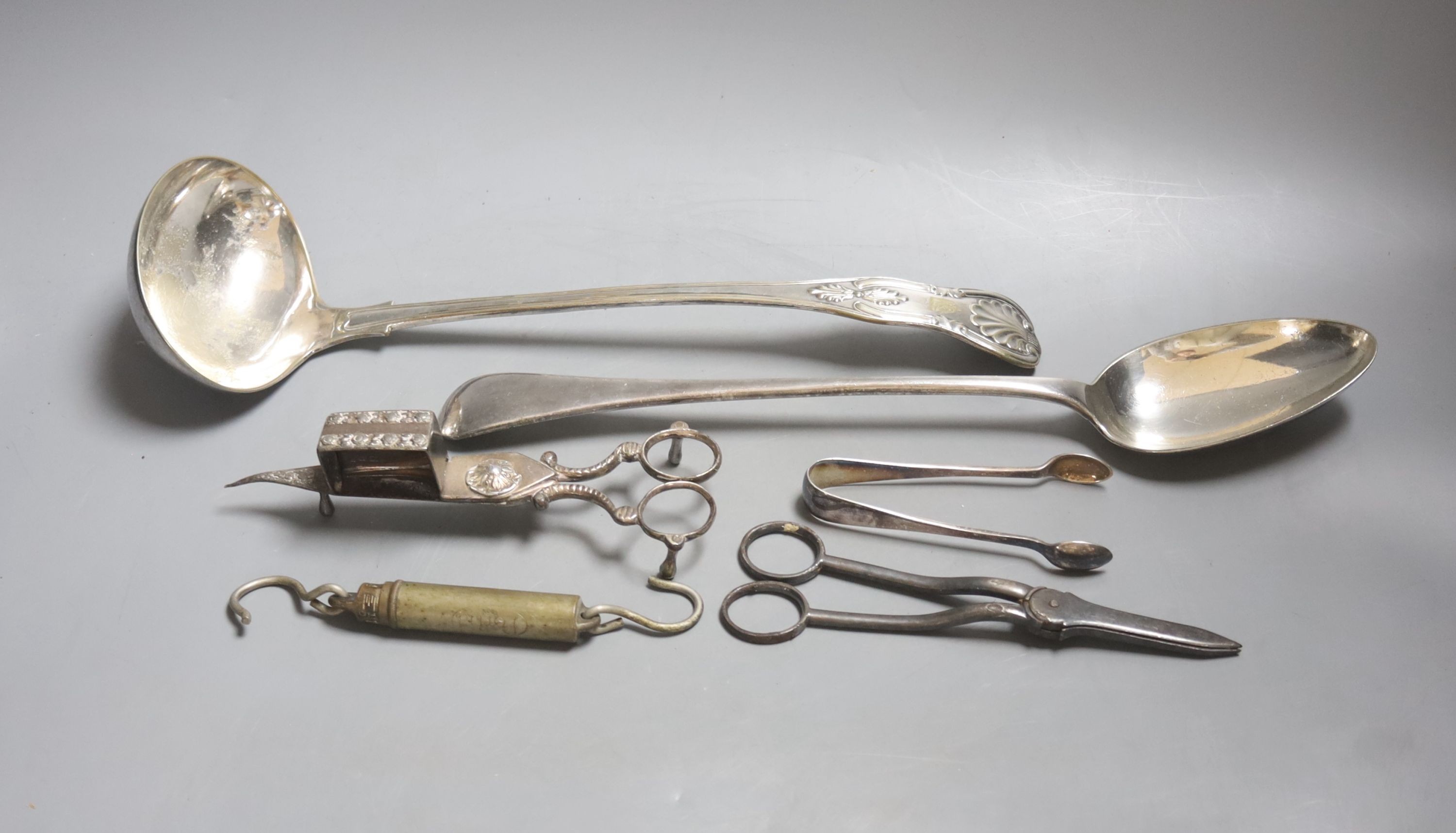 A large plated ladle and basting spoon, two candle snuffers, tongs and spring balance